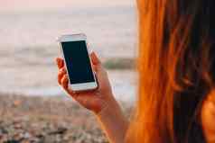 认不出来年轻的女人持有移动电话海滩波海日落社会媒体现代技术夏季假期
