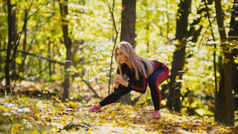 女人健身练习户外女伸展运动秋天森林苗条的女孩锻炼下蹲一边