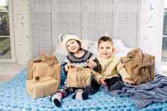 主题圣诞节早....孩子高加索人男孩女孩哥哥妹妹坐着床上拥抱微笑快乐开放一年的礼物盒子阳光明媚的一天