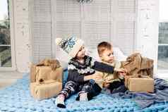 主题圣诞节早....孩子高加索人男孩女孩哥哥妹妹坐着床上拥抱微笑快乐开放一年的礼物盒子阳光明媚的一天