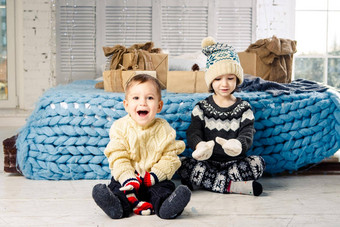 孩子们哥哥妹妹坐地板上卧室床上礼物背景圣诞节装饰阳光明媚的一天穿着温暖的针织羊毛服装帽彩色的连指手套