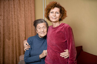 高级高加索人女人温柔拥抱九十年一年上了年纪的妈妈。灰色的头发脸深皱纹首页沙发微笑妈妈。女儿主题护理奉献父母