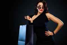 黑色的星期五出售概念商店女人太阳镜持有大袋孤立的黑暗背景购物