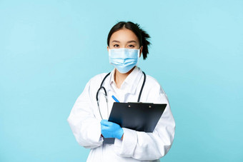 科维德检疫概念微笑亚洲女医生护士脸面具持有剪贴板转变医院站蓝色的背景