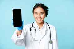网络医疗保健在线概念微笑亚洲女人医生显示智能手机应用程序接口移动屏幕站统一的蓝色的背景