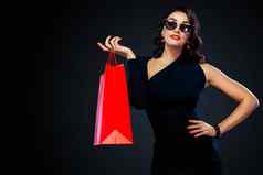 黑色的星期五出售概念商店购物女人太阳镜持有红色的袋孤立的黑暗背景