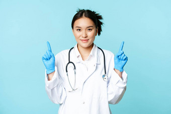 微笑亚洲女医生护士医疗统一的手套指出手指显示医疗保健信息站蓝色的背景