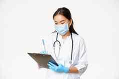 女亚洲医生写作病人信息剪贴板写处方诊断站医疗面具橡胶手套白色背景