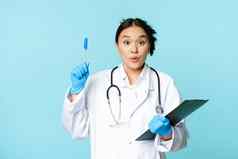 兴奋亚洲女医生持有剪贴板提高笔尤里卡标志启示投手的想法站蓝色的背景
