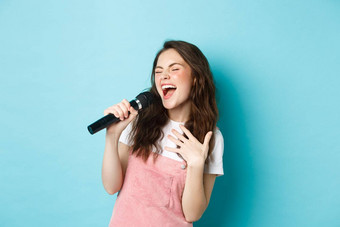 无忧无虑的美丽的女孩执行首歌唱歌麦克风激情玩卡拉ok站蓝色的背景