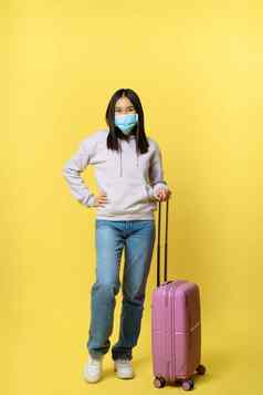 完整的长度拍摄微笑朝鲜文女旅游医疗脸面具摆姿势手提箱假期站黄色的背景