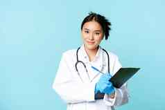 微笑亚洲医疗工人女医生写作病人信息持有笔剪贴板站统一的蓝色的背景