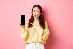 技术在线购物兴奋女孩好奇的点手指空移动电话屏幕显示应用程序智能手机站粉红色的背景