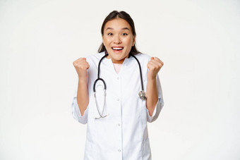 热情的女亚洲医生庆祝充满希望的快乐相机并站医疗统一的白色背景