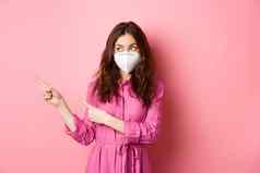 科维德检疫社会距离概念好奇的时尚的女人呼吸器指出手指显示促销文本标志站粉红色的背景