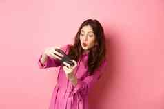 技术概念无忧无虑的年轻的女人倾斜身体持有智能手机水平玩视频游戏电话站粉红色的背景