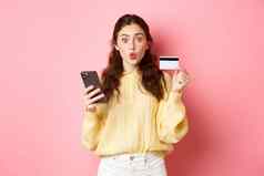 技术在线购物兴奋女孩购物者显示塑料信贷卡持有移动电话支付智能手机订单在线站粉红色的背景