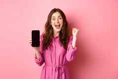 技术概念兴奋女孩显示移动电话屏幕尖叫快乐幸福赢得钱在线实现每天目标智能手机应用程序粉红色的背景