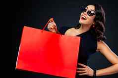 黑色的星期五出售概念商店快乐微笑女孩太阳镜持有大红色的袋孤立的黑暗背景购物女人指出复制空间销售文本