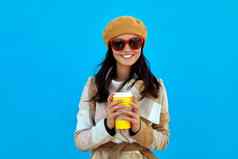 美丽的年轻的女人持有纸杯热咖啡蓝色的背景