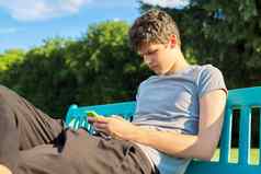 的家伙少年智能手机休息坐着板凳上公园