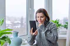 集中成熟的女人智能手机屏幕中年女温暖的毛衣首页冬天雪窗口