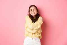 年轻的美丽的女孩感觉健康的快乐拥抱穿软毛衣微笑很高兴站浪漫的粉红色的背景