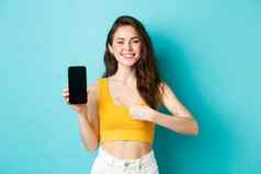 快乐有吸引力的女人显示广告智能手机屏幕指出空显示电话微笑站蓝色的背景