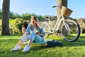 年轻的女人放松坐着草公园智能手机