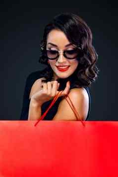 黑色的星期五出售概念商店购物女人太阳镜持有红色的袋孤立的黑暗背景