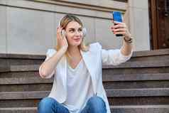 年轻的美丽的女人耳机智能手机休息坐着步骤城市