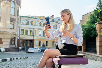 年轻的<strong>业务</strong>女人坐着在户外会说话的视频在线智能<strong>手机</strong>