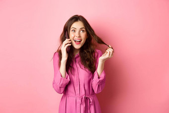 魅力健谈女孩玩头发使订单调用电话会说话的智能手机站粉红色的背景