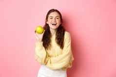 健康的饮食人生活方式概念苹果一天医生女孩持有美味的水果微笑快乐相机站粉红色的背景
