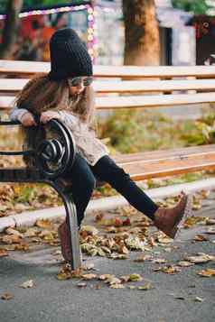 时尚的婴儿女孩一年穿针织他太阳镜靴子皮毛外套坐着板凳上公园相机秋天秋天季节