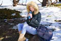 女人喝热金属热水瓶瓶坐着岩石雪山