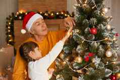 家庭庆祝圣诞节爷爷孩子女孩辫子装修圣诞节树女王白色毛衣高级男人。橙色跳投摆姿势室内节日房间