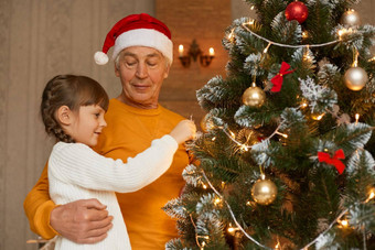家庭装修圣诞节树首页可爱的女孩子穿白色毛衣装修圣诞节树祖父摆姿势室内庆祝一年夏娃