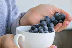 女人持有碗冻蓝莓水果收获概念女手收集浆果健康的吃概念长袜浆果冬天素食者素食主义者食物