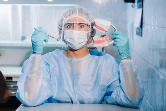 牙科医生穿蓝色的手套面具持有牙科模型上较低的大白鲨牙科镜子