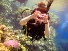 可爱的女孩潜水员显示手手势标志爱心手指合作伙伴教练安全游泳水红色的海珊瑚珊瑚礁埃及沙姆谢赫。