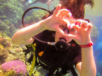 可爱的女孩潜水员显示手手势标志爱心手指合作伙伴教练安全游泳水红色的海珊瑚珊瑚礁埃及沙姆谢赫。