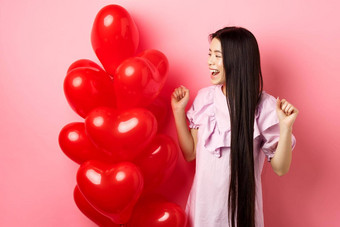 亚洲十几岁的女孩长头发欢呼情人节一天浪漫的礼物标志微笑快乐跳快乐情人礼物<strong>心气球</strong>粉红色的背景
