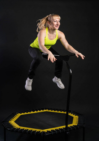 女孩健身蹦床黑色的背景黄色的t恤蹦床跳活跃的身体健身生活方式飞跃可爱的反弹年轻的肌肉教练享受