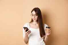 忙女孩眼镜阅读消息移动电话喝咖啡外卖站米色背景