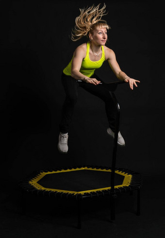 女孩健身蹦床黑色的背景黄色的t恤蹦床适合体育运动锻炼运动员健康的有氧运动锻炼飞中心运动物理肌肉教练享受