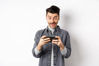 兴奋的家伙玩视频游戏移动电话集中脸利用智能手机屏幕持有手机水平白色背景