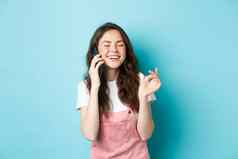 肖像可爱的时尚的女孩笑聊天电话持有智能手机耳朵微笑快乐休闲谈话站蓝色的背景