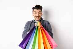 兴奋微笑的家伙持有色彩斑斓的购物袋欢乐折扣商店站白色背景