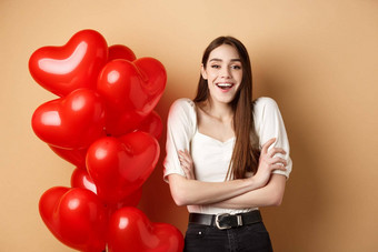 情人节一天概念美丽的年轻的女人有趣的笑微笑相机站浪漫的<strong>心气球</strong>米色背景